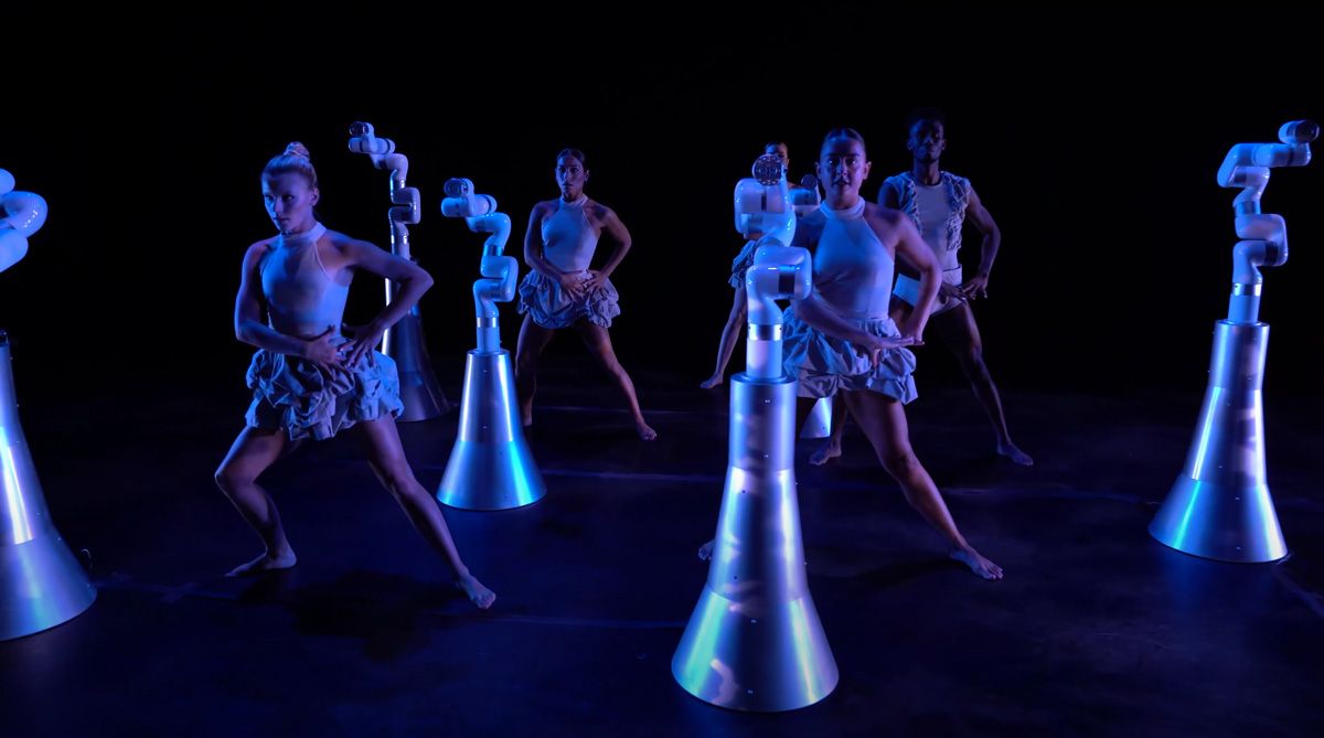 ステージでパフォーマンスを披露する 6 人のダンサーと 6 体のロボット。 