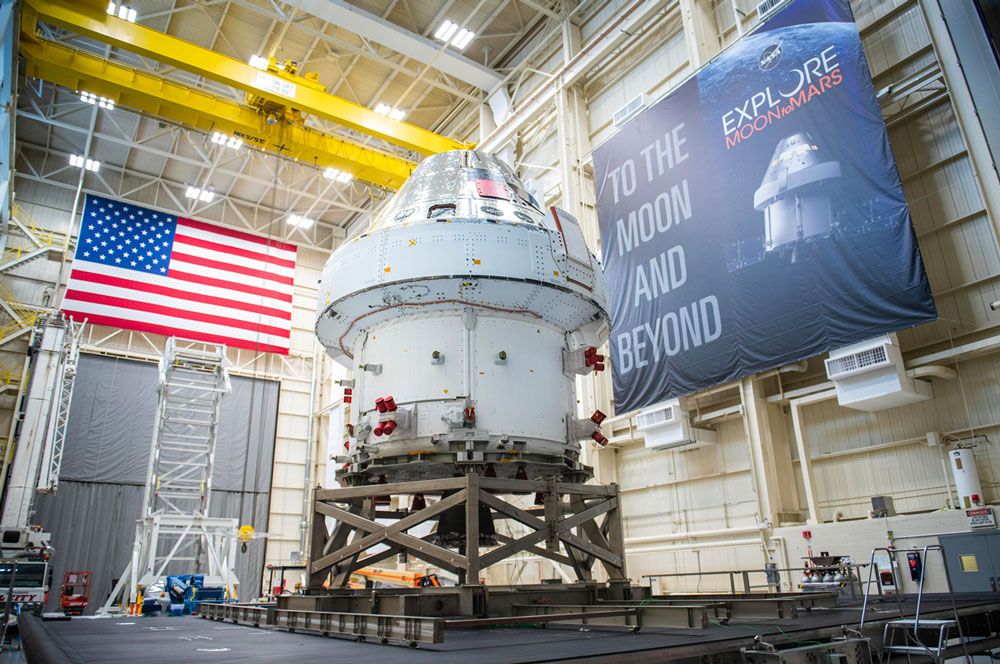 大規模施設内の Orion 宇宙船。壁には米国旗が掲げられ、別の壁には「To the Moon and Beyond」(月へ、そしてさらに遠くへ) という旗が掲げられています。