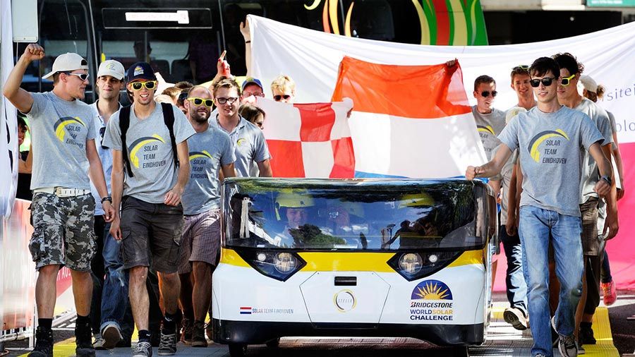 A group of students from Solar Team Eindhoven, including the three Lightyear cofounders, are standing beside the Stella solar car at the 2013 Bridgestone World Solar Challenge.